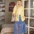 Woman in a yellow shirt and blue skirt standing in a room with a bed and window.